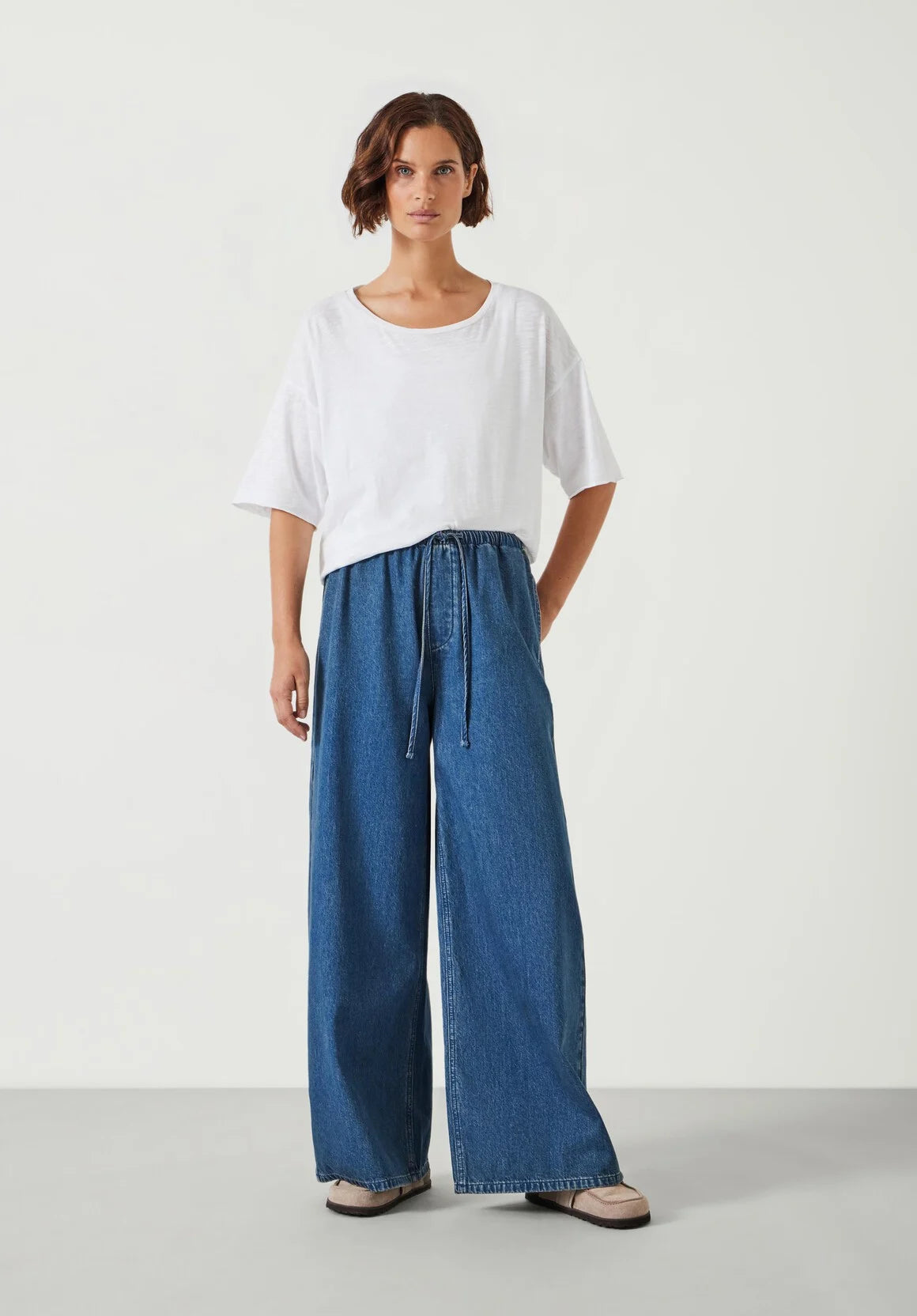 Woman wearing a white top and blue wide-leg pants on a white background