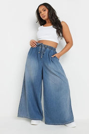 Woman wearing a white crop top and blue wide-leg jeans on a white background