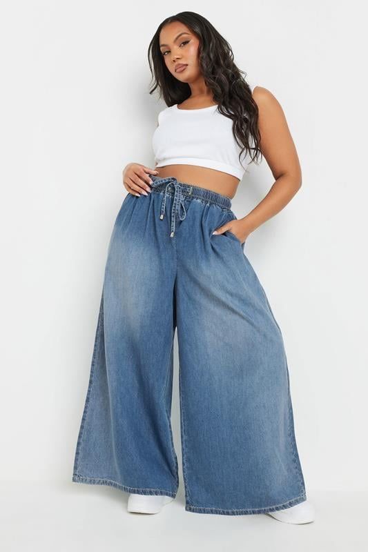 Woman wearing a white crop top and blue wide-leg jeans on a white background