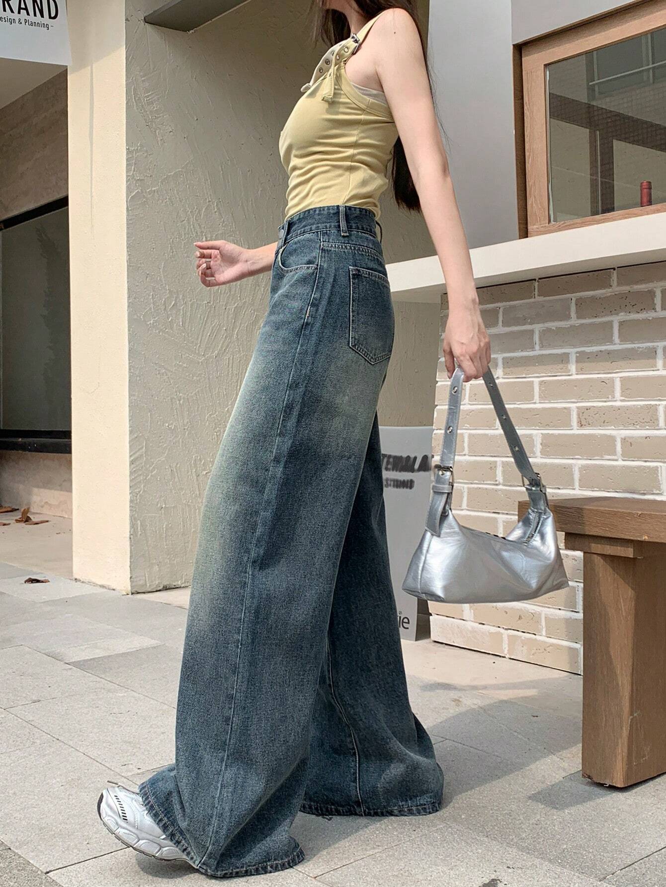 Person wearing a yellow top and blue wide-leg jeans, holding a silver handbag.