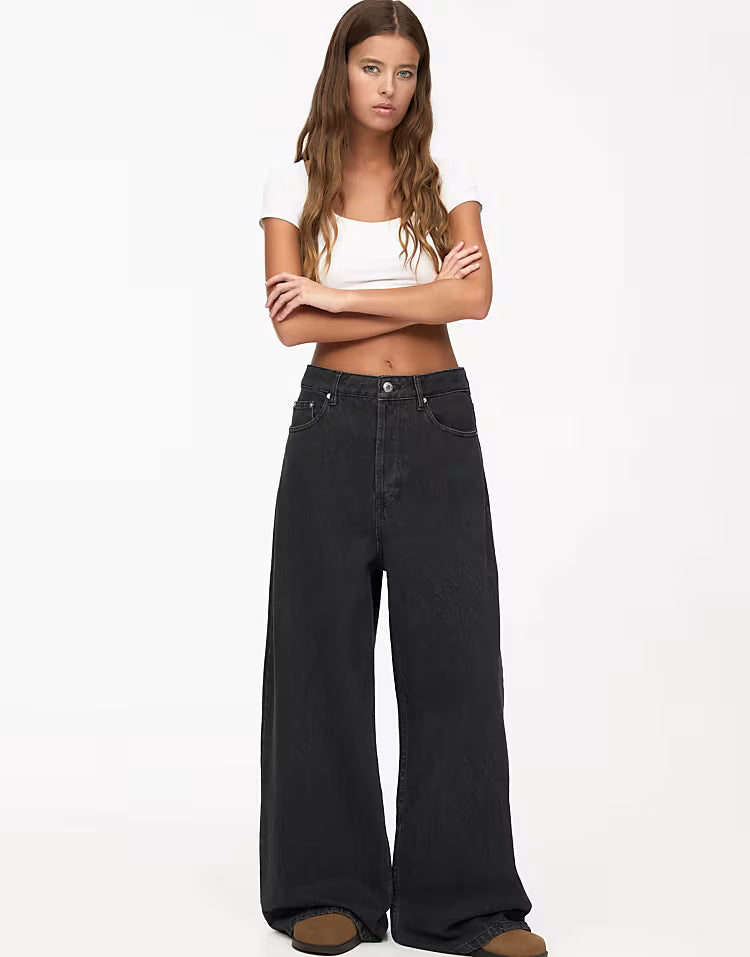 Woman wearing black wide-leg jeans and a white top on a white background