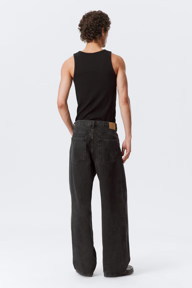 Person wearing a black tank top and dark jeans on a white background