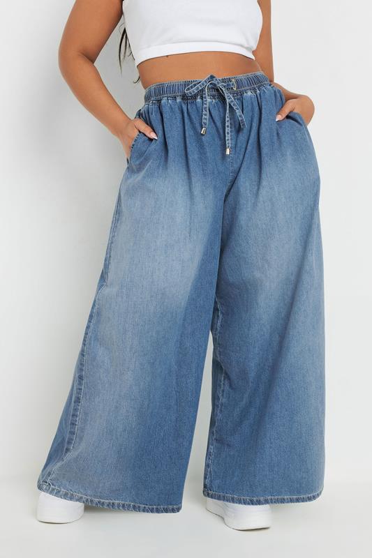 Person wearing wide-leg blue jeans on a white background