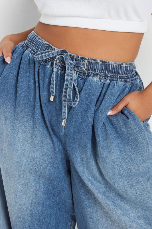 Blue denim pants with a white top on a plain background