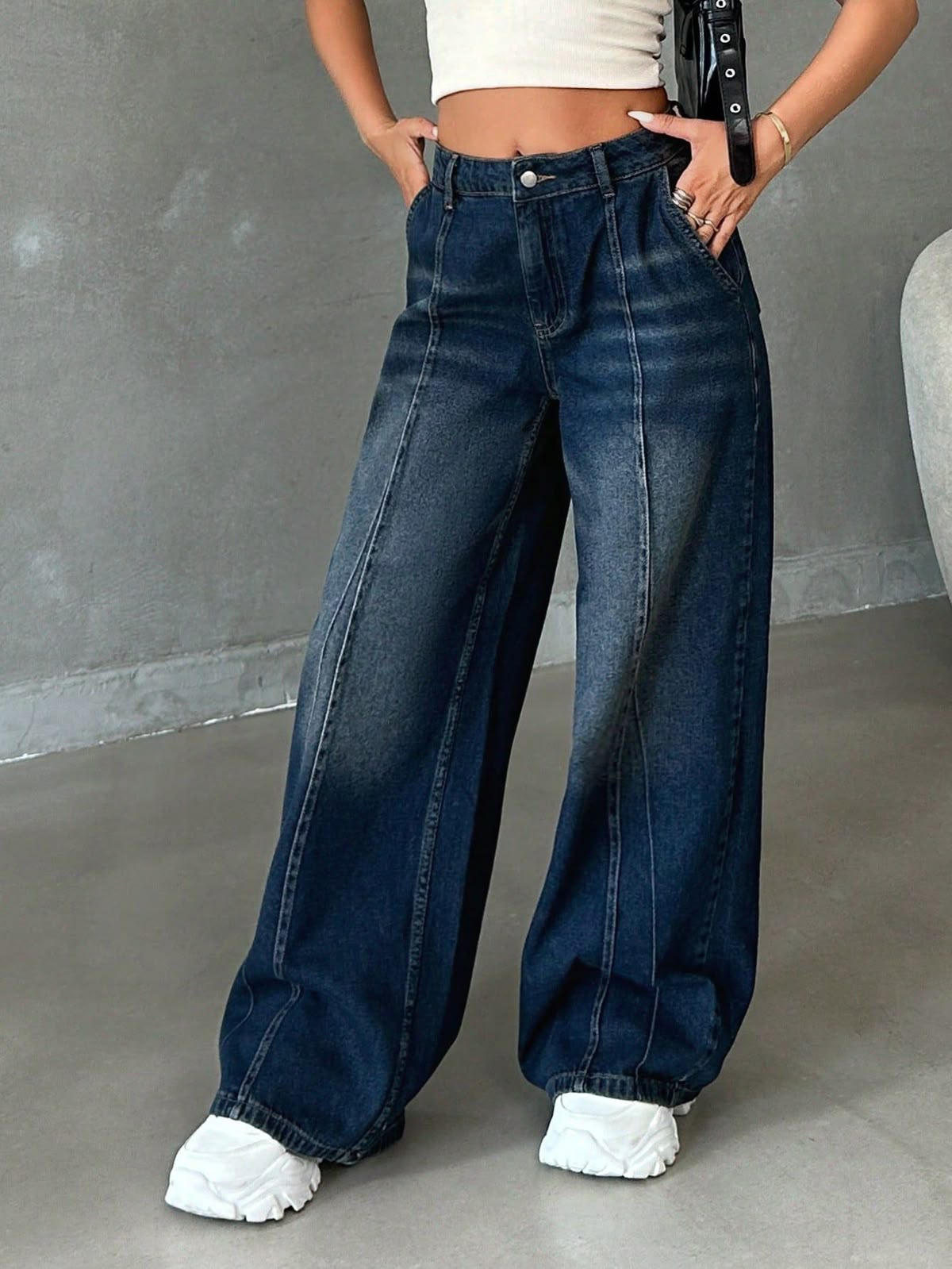 Person wearing wide-leg jeans and white sneakers against a gray background