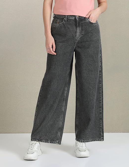 Person wearing black wide-leg jeans and white sneakers on a plain background