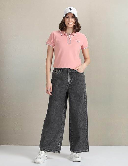 Person wearing a pink polo shirt and black jeans against a neutral background