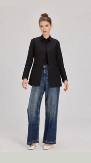 Woman wearing a black jacket and blue jeans on a light gray background