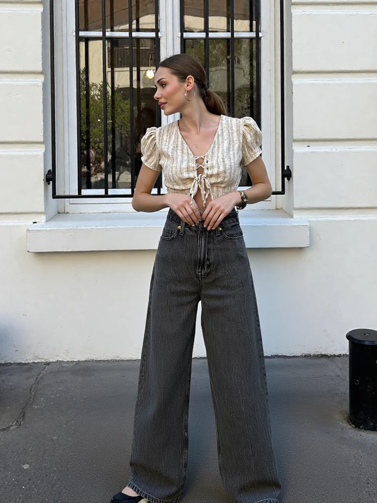 Woman wearing a patterned blouse and high-waisted jeans standing in front of a building.
