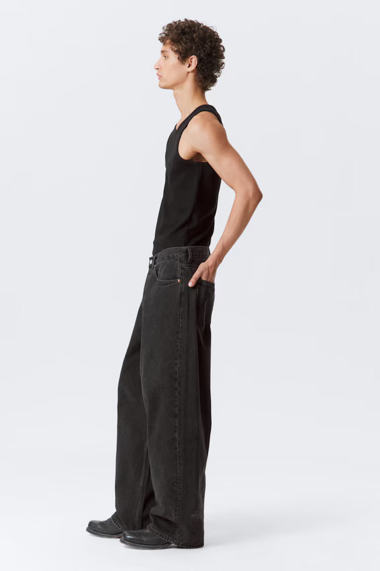 Person wearing a black sleeveless top and wide-leg jeans on a white background